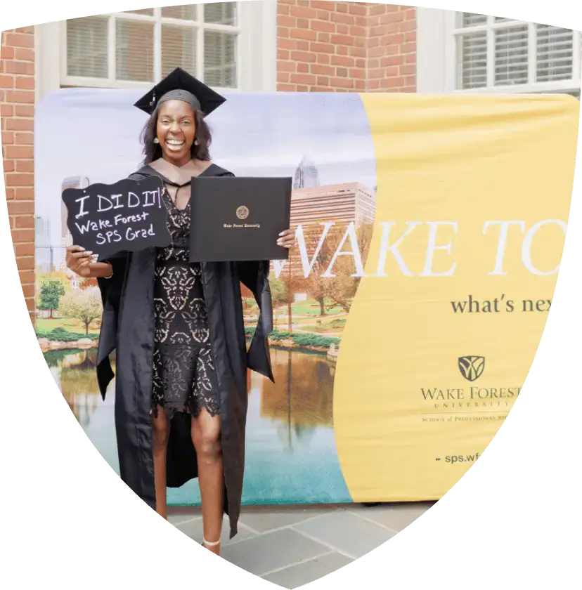 Wake Forest SPS graduate standing in front of WFU signage holding up her degree