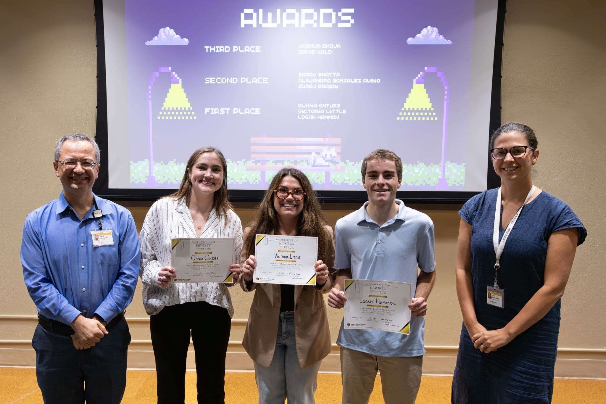 Wake Forest project management students holding their awards in front of a projection screen displaying the award winners.